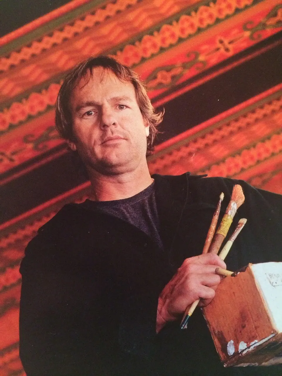 Evan LeGrande Wilson holding brushes and a paint box in front of a polychrome painted ceiling