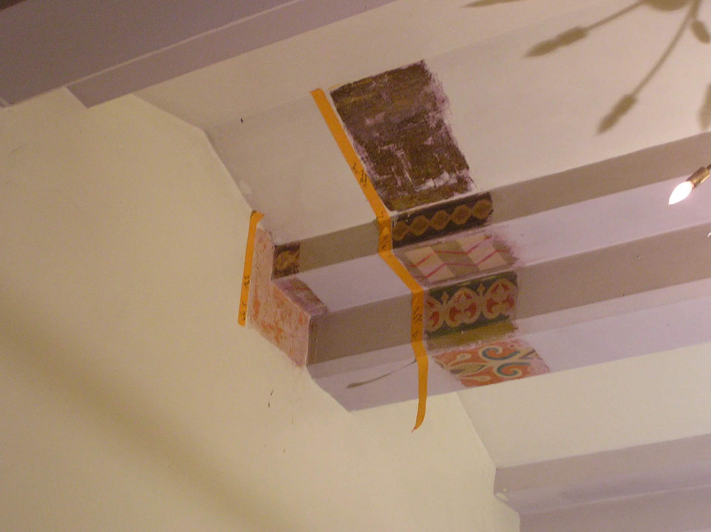 Exposure windows cut through layers of overpaint on a ceiling beam, taped and labelled during paint investigation