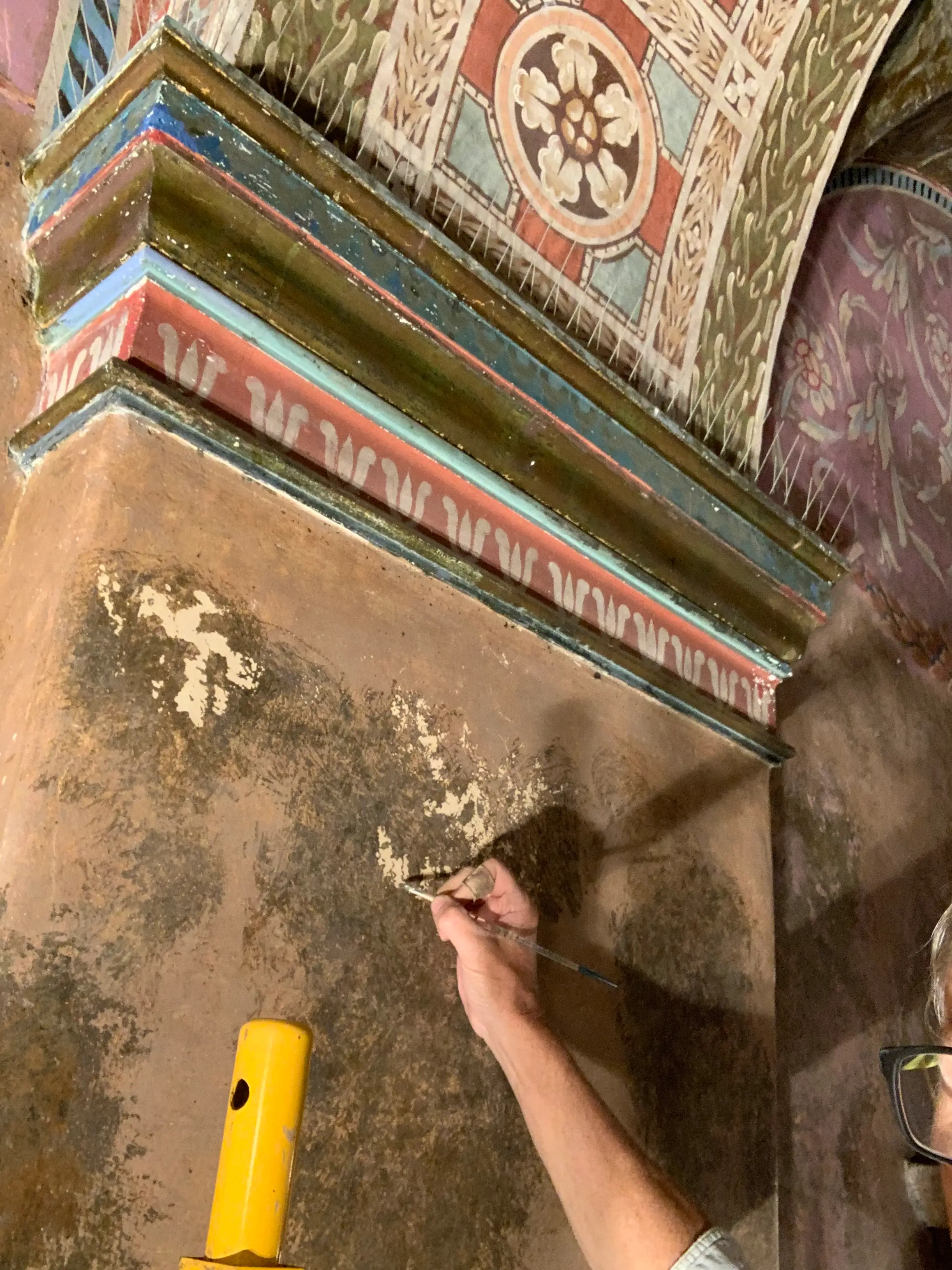 Conservator in-painting a loss on a polychrome decorative cornice with a fine brush